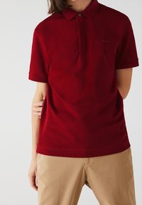 Polo rouge avec col classique, manches courtes et finition subtilement texturée. Présente un petit logo brodé sur la poitrine.