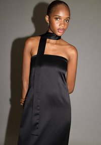 Robe bustier en satin noir avec une longue écharpe attachée au cou. Texture lisse et design minimaliste, ajustée au corps.