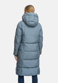Manteau long et bouffant de couleur bleu clair avec une grande capuche, présentant des sections matelassées horizontales et des fentes latérales pour la mobilité.
