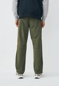 Olivgrüne, leichte Hose mit lockerem Schnitt, sichtbaren Nähten und elastischen Bündchen, kombiniert mit einem grau-schwarzen gestuften Sweatshirt.