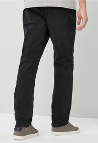 Black denim jeans with a slim fit, featuring two back pockets and subtle textures. Paired with gray casual shoes.
