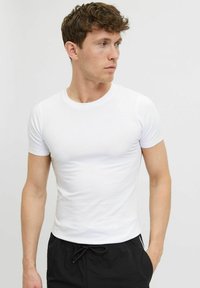 T-shirt blanche à manches courtes avec un col rond, design ajusté et texture lisse, associée à un short noir à cordon de serrage.