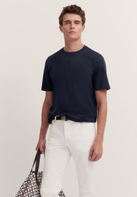 Navy blue short-sleeve t-shirt with a round neckline, paired with white jeans and a patterned tote bag featuring a geometric design.