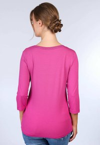 Rosa, langärmliges Oberteil mit rundem Ausschnitt, schlanker Schnitt und glatter Textur, kombiniert mit Jeans. Die Rückansicht zeigt dezente Nähdetails.