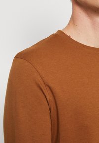 Langermet skjorte i en varm brunfarge, laget av et mykt og glatt stoff, med rund hals og klassisk passform.