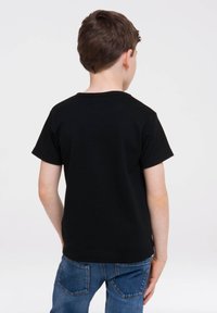 Black cotton T-shirt with short sleeves, round neckline, and a smooth texture, worn by a child facing away. Paired with blue denim jeans.
