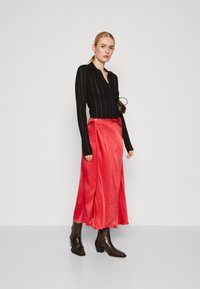 Svart ribbet langermet skjorte som er parret med et rødt satin maxiskjørt, med en sideslitt. Modellen har på seg brune blokkhelte støvler.