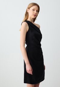 Abito nero a spalla unica in un design aderente, realizzato in un materiale liscio con una leggera texture e dettagli drappeggiati.
