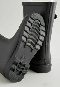 Schwarzer wasserdichter Gummistiefel mit einer strukturierten Grip-Sohle, glatter Oberfläche und einer abgerundeten Spitze. Keine auffälligen Akzente oder Muster vorhanden.
