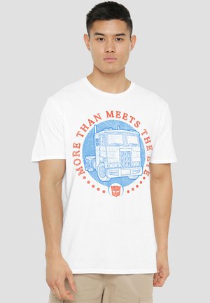 Weißes Baumwoll-T-Shirt mit einem blauen Grafik eines Lastwagens, rotem, kreisförmigem Text "MEHR ALS MAN AUF DEN ERSTEN BLICK SIEHT" und einem kleinen Logo am unteren Ende.