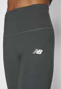 Leggings grigi scuri realizzati in un tessuto testurizzato con vita alta, con logo bianco a contrasto sul lato sinistro e cuciture piatte.