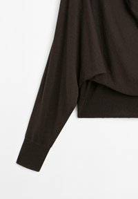 Brown oversized long-sleeve top with a textured, ribbed hem and cuffs. Draped design with a relaxed fit and side slits at the bottom.