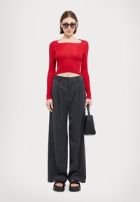 Red ribbed long-sleeve top with cut-out neckline, paired with high-waisted gray trousers. Black handbag and chunky open-toe sandals included.