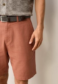 Rustfarvede linnedshorts med sidelommer, parret med en struktureret grå skjorte med knapper og et flettet sort bælte med sølvspænde.
