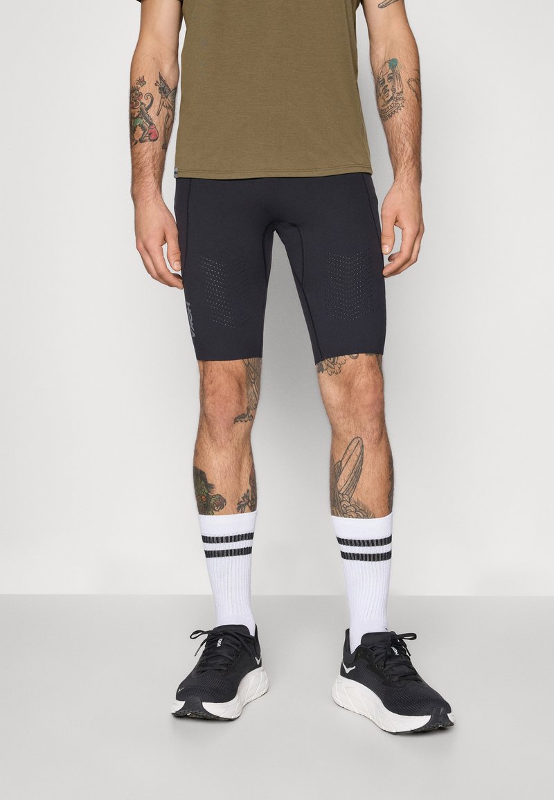 Kurze sportliche Shorts in Schwarz mit durchbrochenem Design, kombiniert mit weißen Socken mit schwarzen Streifen und schwarzen Laufschuhen.