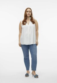 Haut sans manches blanc à décolleté en V profond, associé à un jean taille haute bleu clair et des escarpins à talons sling-back bleus ornés d'un accent floral.