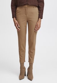 Braune maßgeschneiderte Hose in Slim-Fit, mit glatter Textur, vorderen Taschen und cropped Länge, kombiniert mit passenden High-Heels.