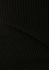 Gros plan sur un tissu tricoté côtelé noir montrant la texture et des motifs de couture verticaux avec un léger pli diagonal.