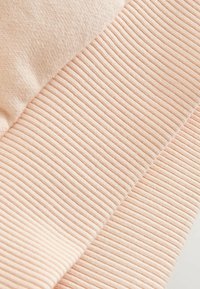 Gros plan sur un tissu en maille beige côtelé avec une couture diagonale visible sur un matériau à texture douce.