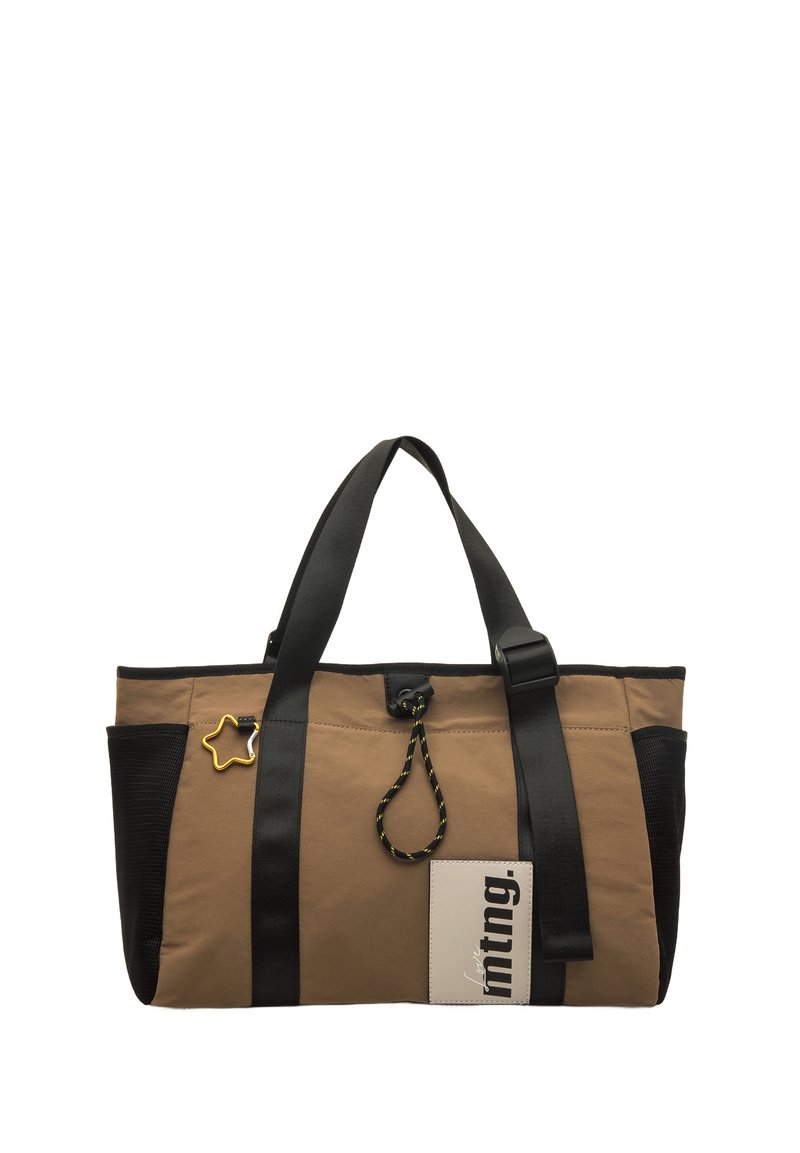 Tote bag in beige en zwart, vervaardigd uit stevig materiaal, met een afneembare stervormige charm en contrasterende banden met een voorlabel waarop tekst staat.