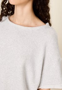 Pilkos spalvos trumpomis rankovėmis megztinis su plačiu ir apvaliu kaklu. Minkšta, tekstūruota medžiaga su matomomis siūlėmis aplink apykaklę ir apatinę dalį.