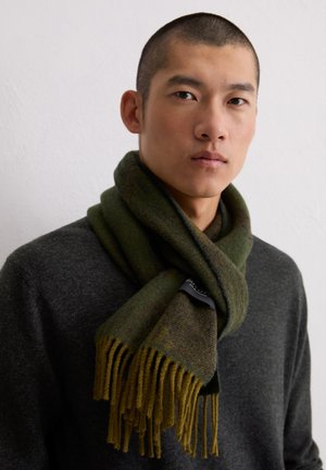 Écharpe vert olive en laine douce, avec un mélange de textures et de longues franges, portée sur un pull gris foncé.