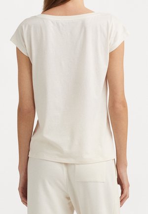 Mujer con una camiseta blanca lisa de manga corta y pantalones blancos a juego, vista por detrás sobre un fondo liso.