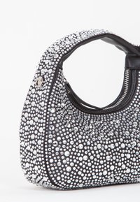 Sac à main noir de forme arrondie, couvert de clous irisés de différentes tailles, avec une fermeture éclair et une poignée solide.