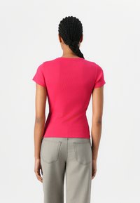 T-shirt rose ajusté en maille côtelée à manches courtes et col rond, associé à un pantalon gris taille haute avec poches arrière.