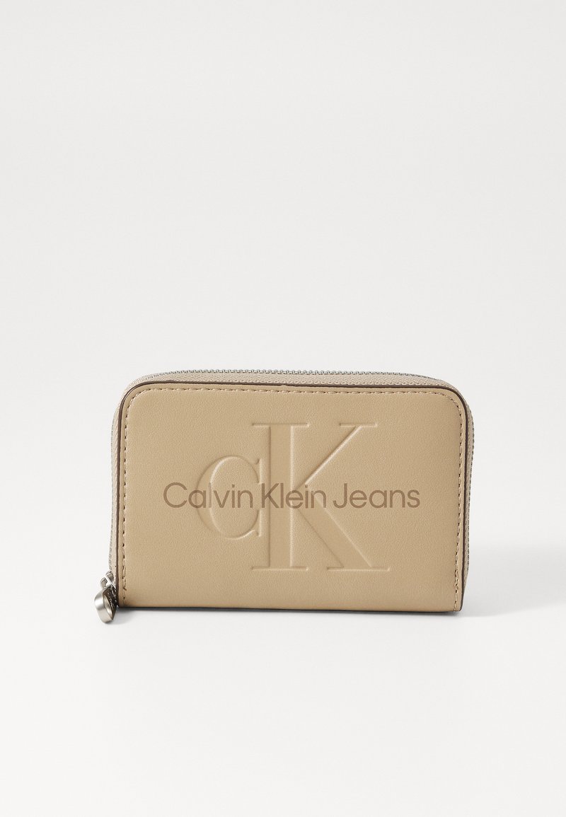 Smėlio spalvos odinė piniginė su iškilusiu "CK" logotipu ir "Calvin Klein Jeans" užrašu. Turi užtrauktuko uždarymą ir lygią tekstūrą.
