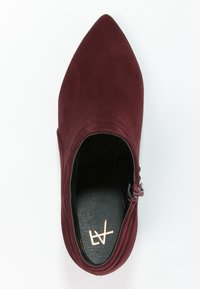 Burgundowe zamszowe botki za kostkę z wydłużonym noskiem, zamkiem błyskawicznym po bokach oraz gładką czarną wkładką z logo.