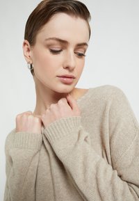 Maglione beige lavorato a maglia con polsini a costine. Texture morbida, vestibilità leggermente ampia e collo casual. Le pieghe sulle spalle creano un aspetto rilassato.