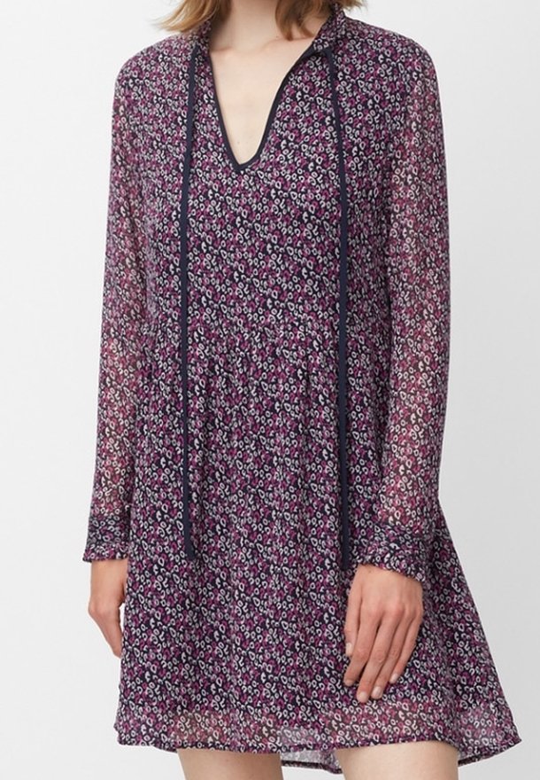 Lila blomklänning med långa ärmar, djup V-ringning och kontrasterande marinblå band. Har en lätt, genomskinlig tyg och inringad midja.