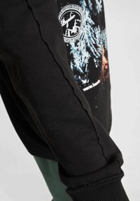 Melnā sporta krekls ar teksturētu virsmu, kas piedāvā unikālu šuvju detaļu gar piedurkni un krāsainu grafiku uz aizmugures.