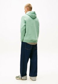 Myntrgrøn hoodie med en afslappet pasform, mørkeblå jeans og lys grå opkrøllede ærmer, båret med afslappet fodtøj.