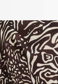 Motif abstrait tourbillonnant et parsemé de points, dans des tons brun foncé et beige, évoquant des motifs inspirés de la faune ou de la nature sur un tissu.