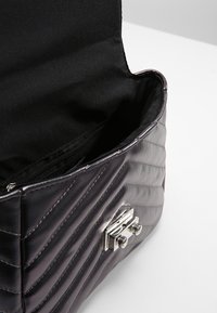Borsa a tracolla in pelle nera trapuntata con una chiusura argento lucido, dotata di una tasca con zip all'interno e di un'esterno liscio e texturizzato.