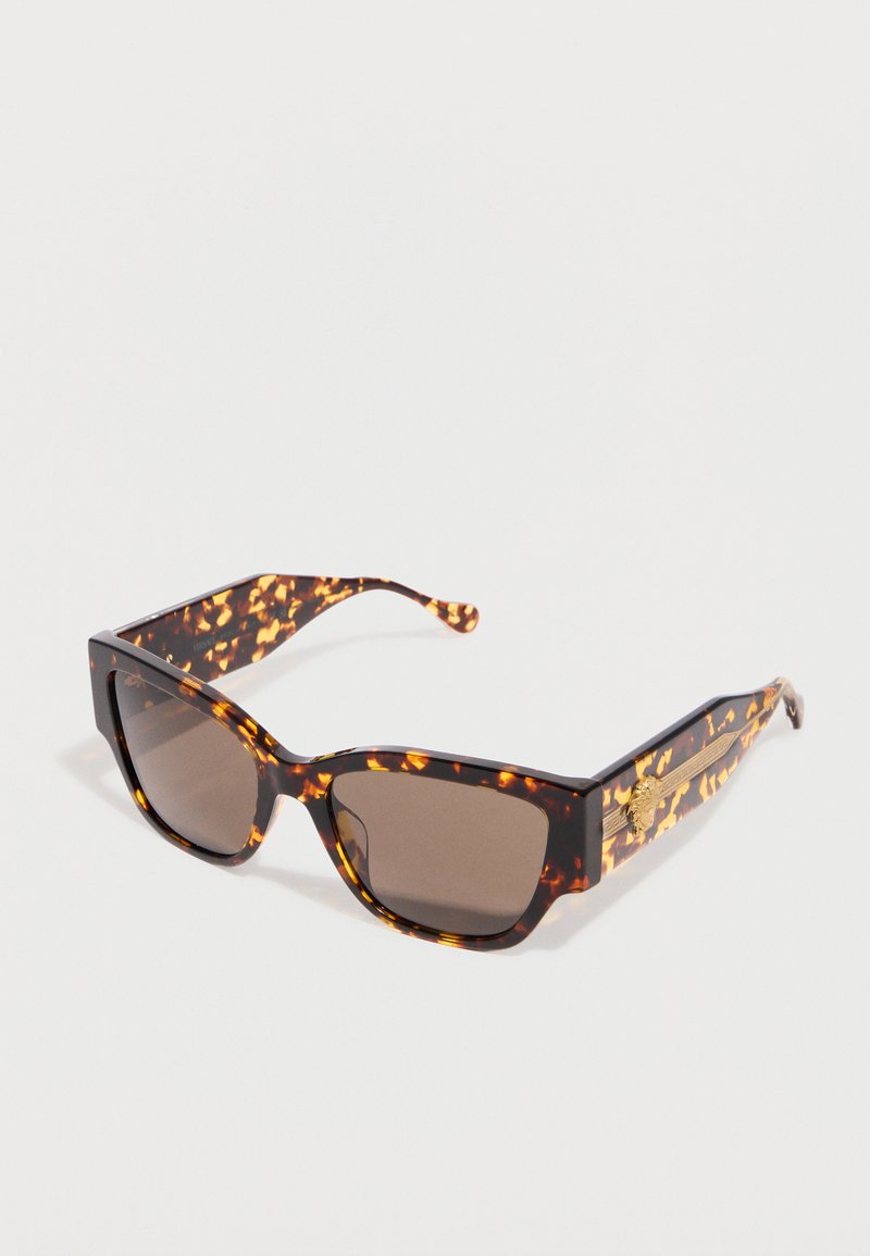 Lunettes de soleil rectangulaires écaille de tortue avec verres foncés et emblème décoratif doré sur de larges branches, inclinées sur fond blanc.