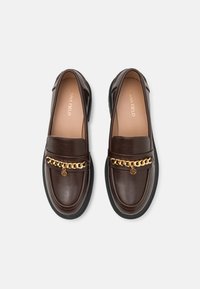 Brown leather loafers with a gold chain accent, round toe, and a thick black rubber sole. Smooth texture with stitched detailing.