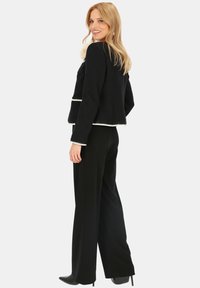 Czarna krótka kurtka z białymi wykończeniami, zestawiona z czarnymi szerokimi spodniami. Tkanina wydaje się teksturowana; kurtka ma strukturalny krój.