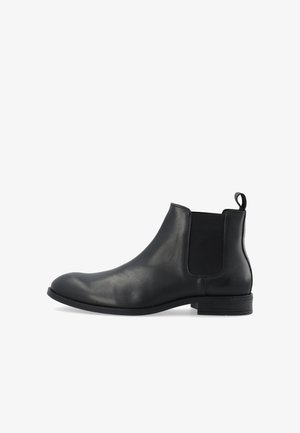 Botte Chelsea en cuir noir avec panneaux latéraux élastiques, languette au talon, talon bas empilé et bout arrondi sur fond blanc.