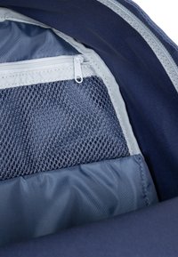 Interiér námořnického batohu s kapsou ze síťoviny na zip, hladkou látkovou podšívkou a texturovaným zipem na oddělení se světle šedým akcentem.