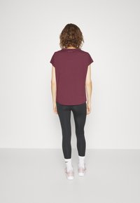 Burgundy t-shirt med kort ärm och rundad nederkant, kombinerad med svarta leggings och ljusrosa sneakers. Enkel design; inga synliga grafik eller mönster.
