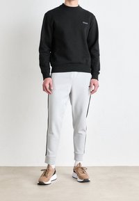 Felpa nera con scollo rotondo, polsini a coste, abbinata a pantaloni jogger grigi con strisce laterali nere. Scarpe da ginnastica color cuoio e nero completano il look.