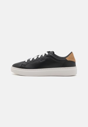 Schwarzer Sneaker mit niedrigem Schaft, weißen Schnürsenkeln, weißer Sohle und beige Wildleder-Fersenlasche, von der Außenseite auf einfarbigem Hintergrund gezeigt.