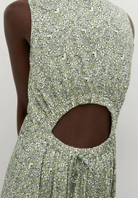 Robe florale verte avec un corsage ajusté, design sans manches et dos découpé. Comprend une taille élastique et des motifs floraux blancs.