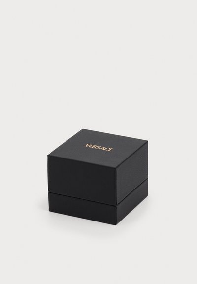 Scatola regalo quadrata nera con una superficie texture e una leggera lucentezza, che presenta il logo dorato "VERSACE" sulla parte superiore. Chiuso senza hardware visibile.