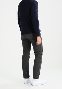 Pantalon gris foncé à coupe fuselée, ourlets retroussés, associé à un pull à manches longues bleu marine et des baskets blanches. Texture de tissu lisse.