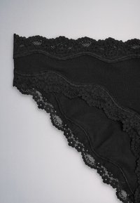 Black lace-trimmed women's underwear with floral lace patterns along waistband and leg openings on a gray background.