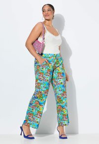 Blå mönstrade byxor med en livlig design som har blommönster och grafiska inslag; kombinerat med en vit texturerad topp och en rosa väska.